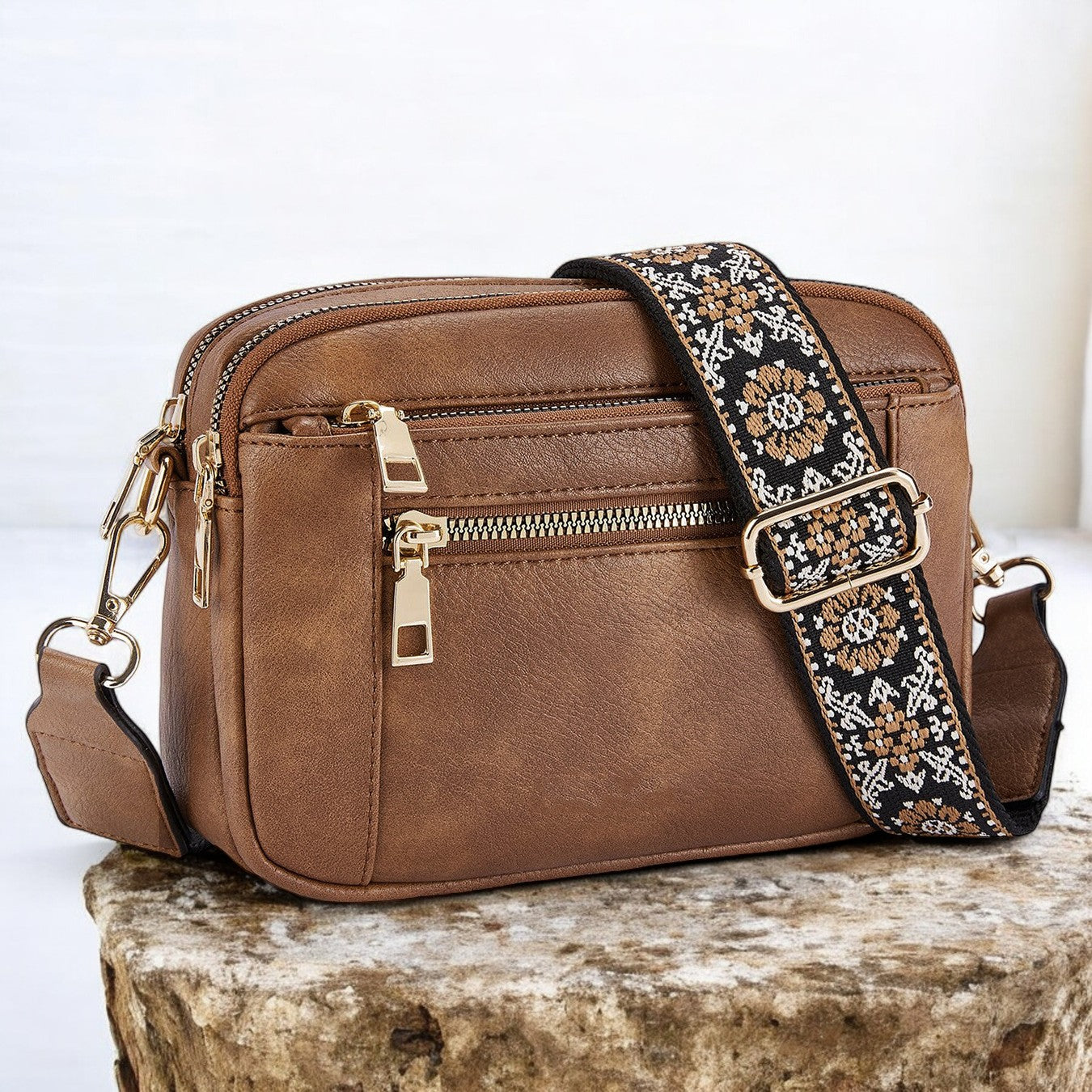 Brown leather crossbody bag with a decorative strap on a stone surface